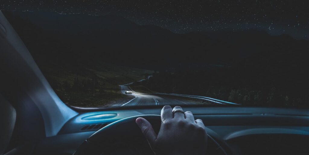 Derselbe Blick bei Nacht: Straße im Scheinwerferlicht, entgegenkommendes Auto, Sternenhimmel